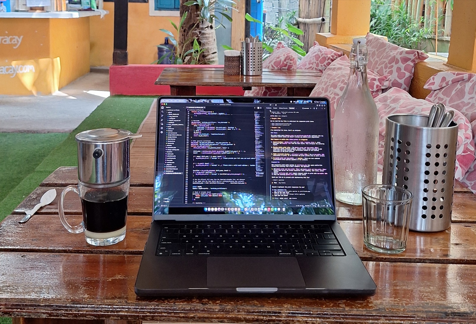 A laptop displaying code on a wooden table beside a cup of black coffee in a cafe