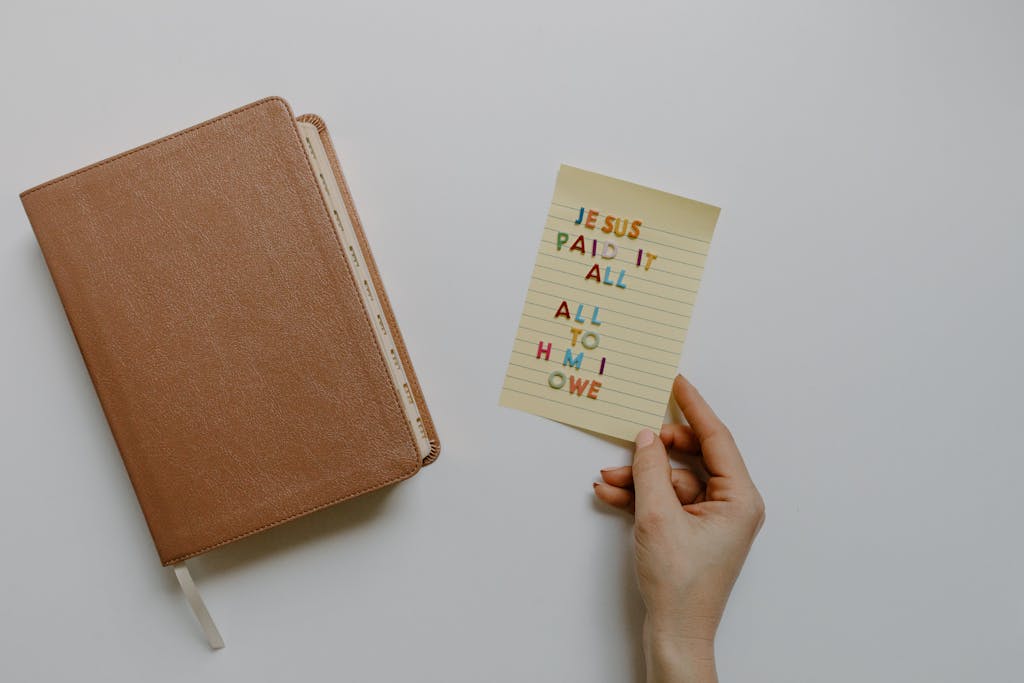 Bible with a note saying 'Jesus paid it all, all to Him I owe' on a clean background.