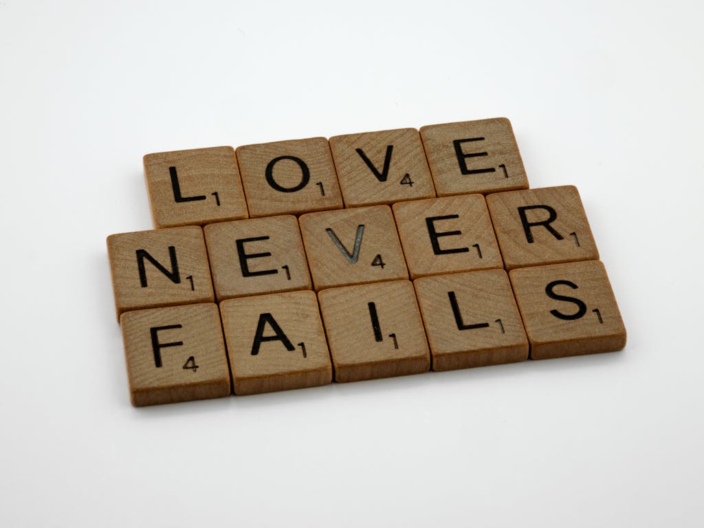 Wooden Scrabble tiles spelling out 'Love Never Fails' on a white background.